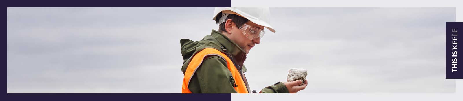 Geologist outside wearing PPE looking at a rock he's holding.